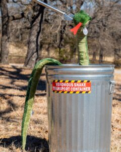 a humorous photo of a fake toy snake being placed within a tin trashcan labeled for venomous snakes.